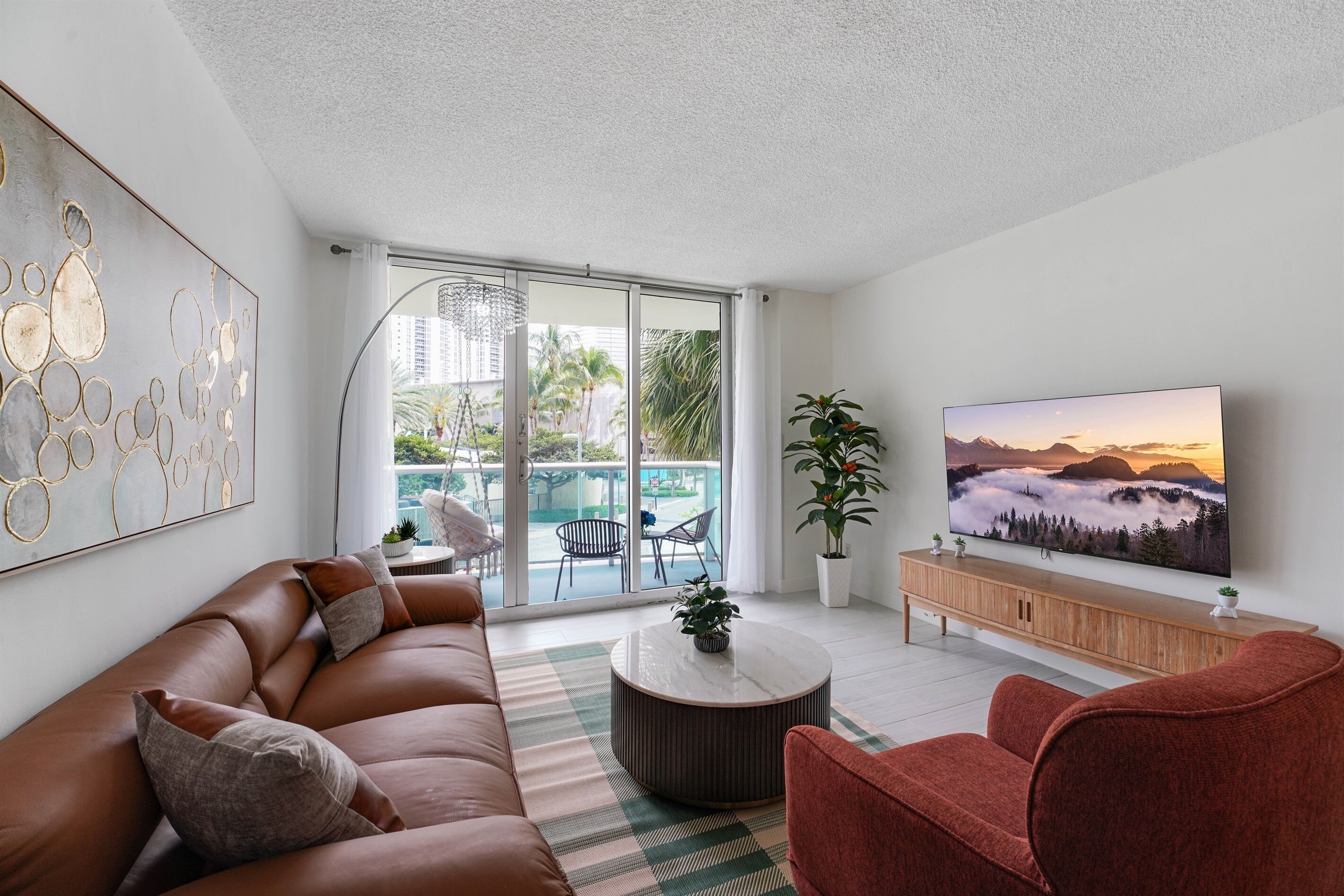 Una sala de estar moderna con sofá, sillones, una mesa de centro, televisor y un balcón con mobiliario exterior.