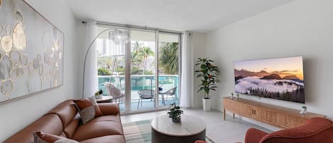 Una sala de estar moderna con sofá, sillones, una mesa de centro, televisor y un balcón con mobiliario exterior.