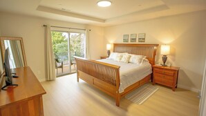 A bedroom with a wooden bed, a nightstand, a desk, and a sliding glass door leading to an outdoor area. - Townhouse on the Trail (Sequim)