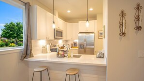 A modern kitchen with white cabinetry, a stainless steel refrigerator, and pendant lighting. - Townhouse on the Trail (Sequim)