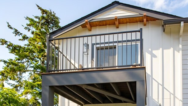 A two-story house with a balcony, a front door, and a small garden with various flowers. - Townhouse on the Trail (Sequim)