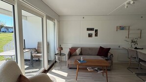 Een moderne woonkamer met een bank, salontafel en fauteuil, grote ramen en uitzicht op de omgeving.