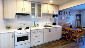 A modern kitchen with white cabinets, a built-in microwave, and a dining area with a wooden table and chairs. - Bonnie 1 Cottage/Resort/Orillia, Muskoka (Washago)