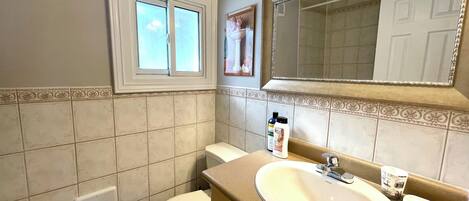 A bathroom with a toilet, sink, mirror, and window.
