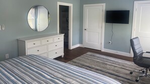 A bedroom with a bed, dresser, mirror, ceiling fan, TV, and a door leading to a closet.