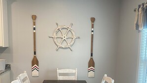 A dining room with a long wooden table, white chairs, and two decorative wooden paddles on the wall.