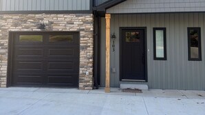A two-story house with a garage, stone foundation, and a front door with a number plaque.