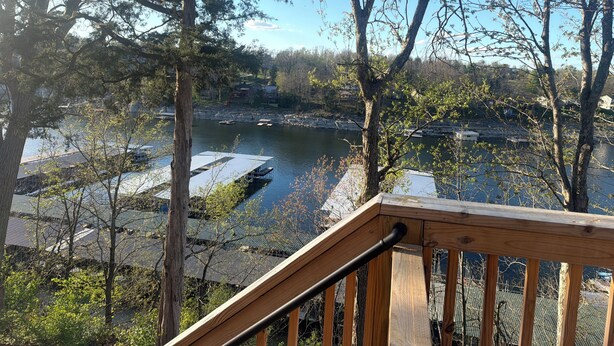 A wooden deck with a railing overlooking a body of water, surrounded by trees and buildings.