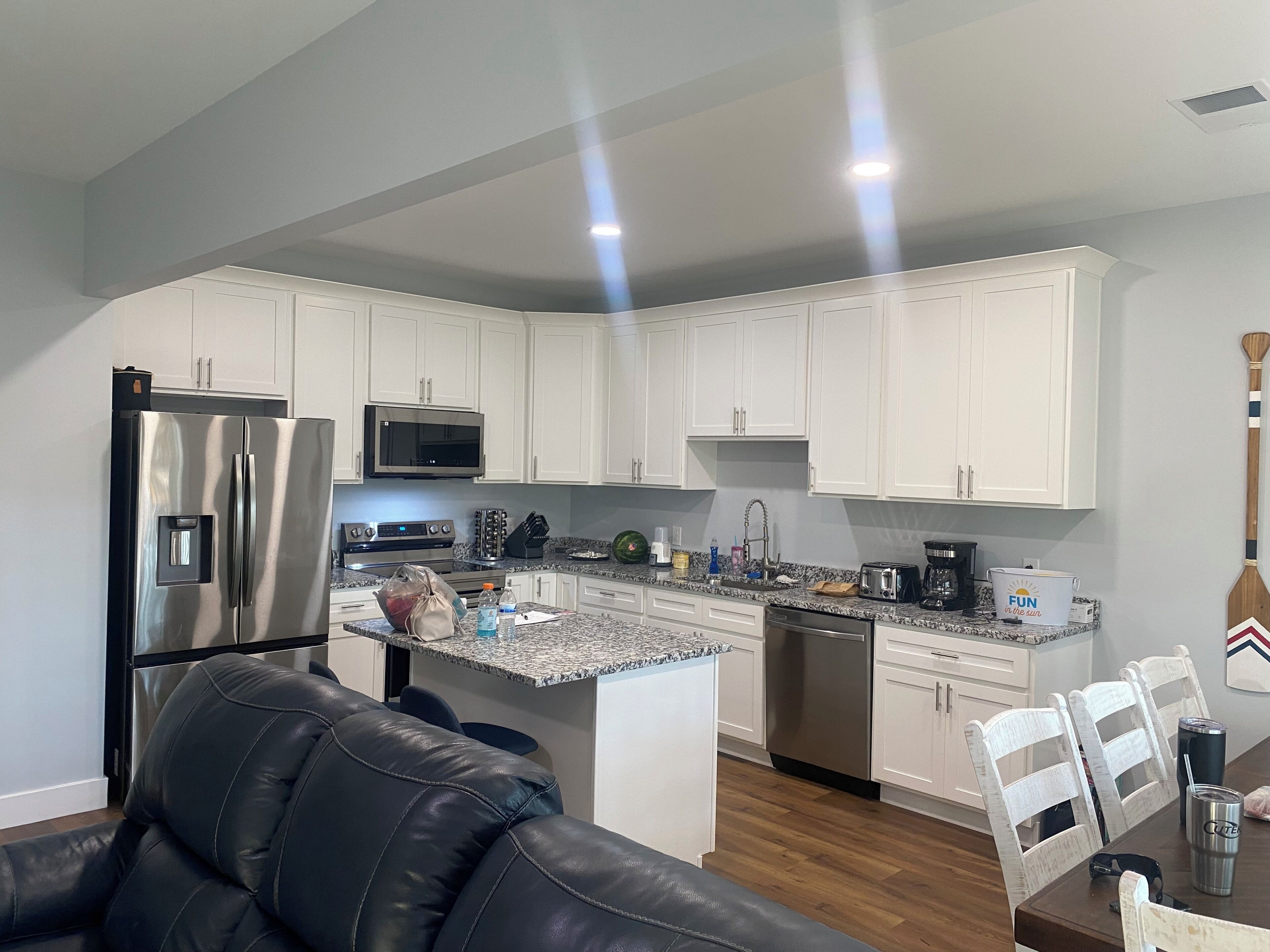 Una cocina moderna con armarios blancos, electrodomésticos de acero inoxidable, encimera de granito y comedor con mesa y sillas de madera.