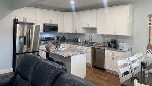 A modern kitchen with white cabinets, stainless steel appliances, a granite countertop, and a dining area with a wooden table and chairs.