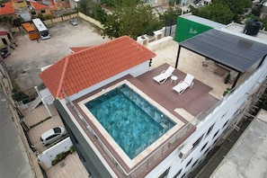 Une piscine sur le toit, avec un toit rouge, entourée de chaises longues et d’une petite table.