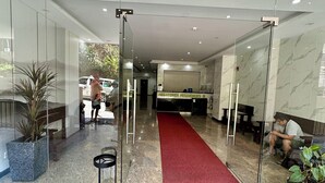 Una hall d'albergo con tappeto rosso, pavimento in marmo, pareti in vetro e una reception.
