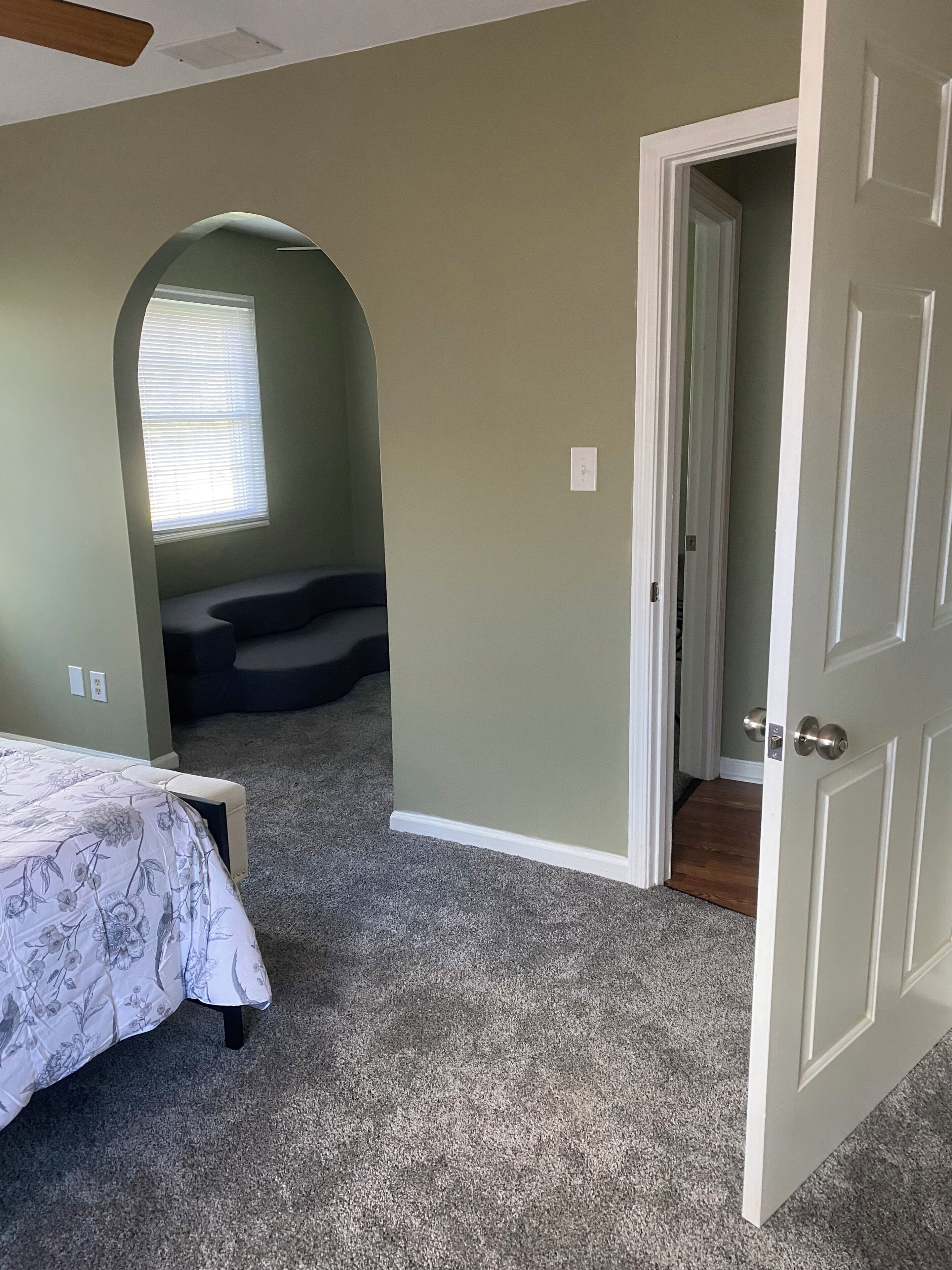 A bedroom with a bed, a window with blinds, a door, and a carpeted floor.