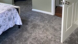 Un dormitorio con cama, ventana con persianas, puerta y piso cubierto de alfombra.