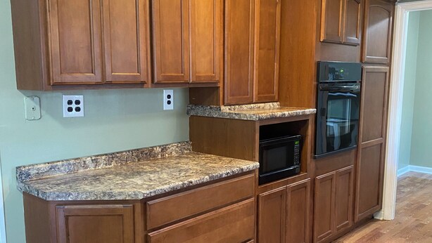 Una cocina con armarios de madera, encimera de granito, horno empotrado y refrigerador.