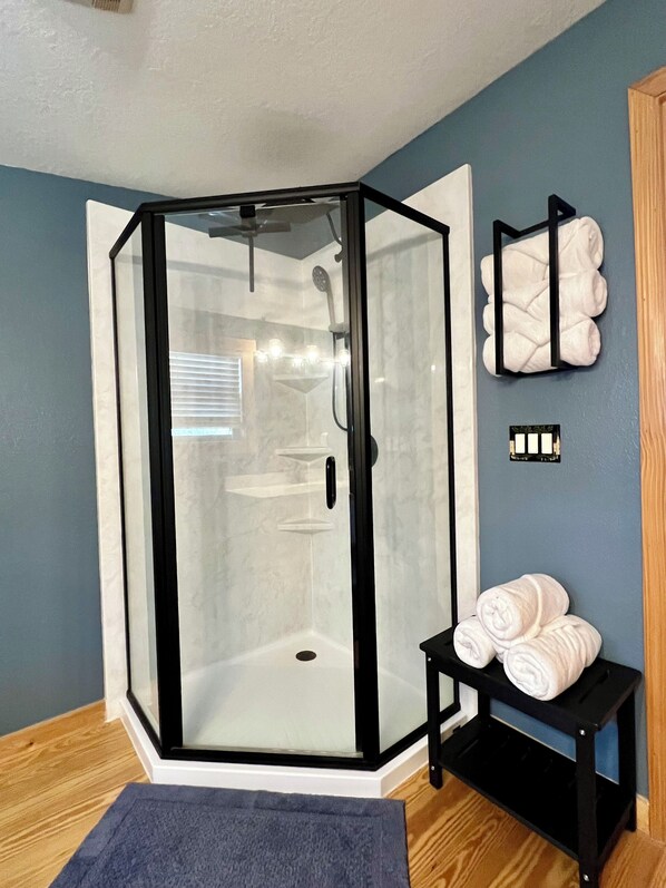 A glass-enclosed shower with a white door, a towel rack with towels, and a small table with towels. - Meadow Vista – 3BR/3BA Cabin Nestled in the Blue Ridge Mountains (Murphy)