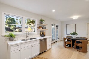 Una cocina con armarios blancos, un lavamanos y una zona de comedor con mesa y sillas.