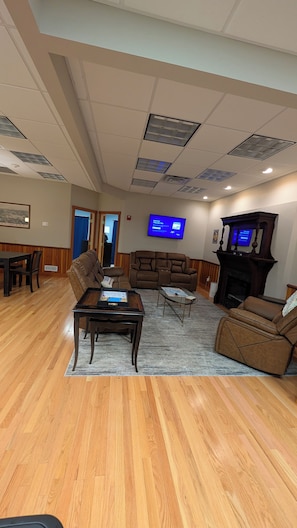 A spacious living room with a wooden floor, a brown leather sofa, a glass coffee table, and a fireplace. - 3BR Gilford Condo, Newly Updated, 2 private balconies, 2 min to walk town docks. (Gilford)