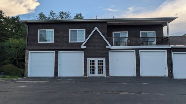 A two-story building with a dark exterior, white garage doors, and a balcony on the upper floor.