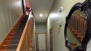 Ein Flur mit einem Schachbrettmuster auf dem Boden, einer Holztreppe, einem Wandspiegel und einer Tür am Ende.