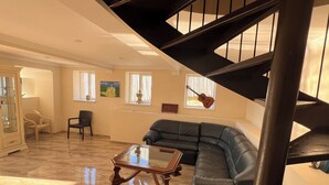 A spacious living area with a black staircase, a leather sofa, a glass-top coffee table, and a dining table. - Happy house (Kutaisi)