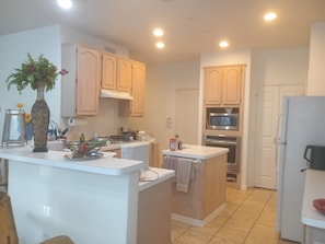 A modern kitchen with white countertops, wooden cabinets, a central island, a microwave, oven, and a refrigerator. - Spacious 5-bedroom house with pool by Six Flags in beautiful Arlington (Arlington)