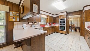 A kitchen with wooden cabinets, a white countertop, a built-in oven, and a dining area visible through an open doorway.