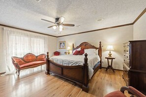 Une chambre à coucher avec un lit en bois, un ventilateur de plafond, une table de chevet, une chaise et une commode.