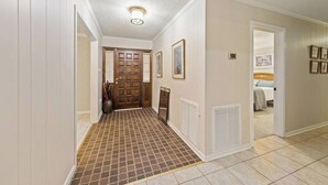 A hallway with a patterned floor, a wooden door, and a bed visible in the adjacent room.