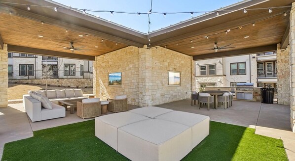 An outdoor living area with a stone wall, a white sofa, a dining table, and ceiling fans.