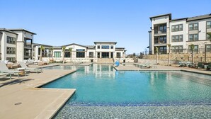 Uma piscina com espreguiçadeiras, um edifício com telhado plano e céu claro.