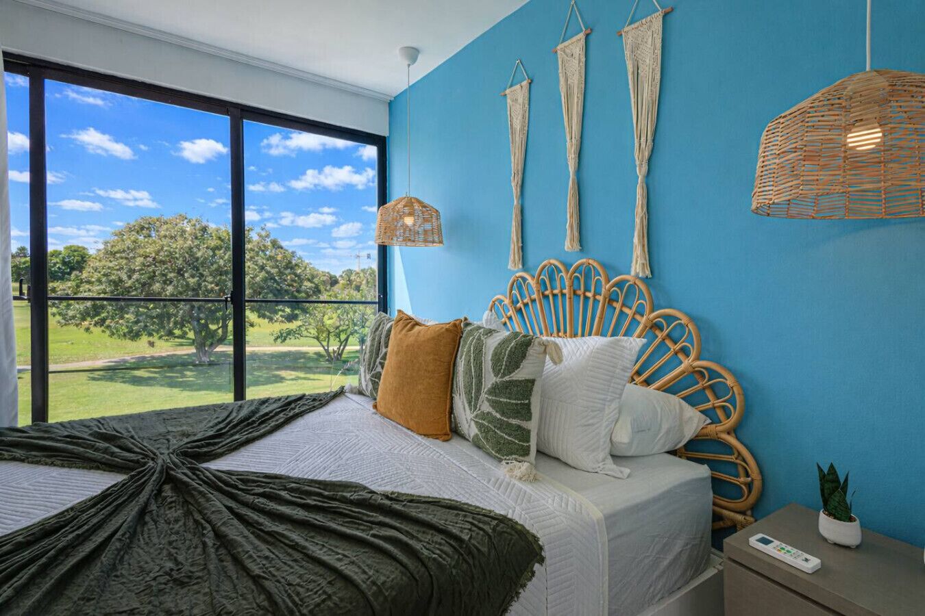 A bedroom with a bed, pillows, a headboard, a hanging light, a window, and a view of the outdoors.