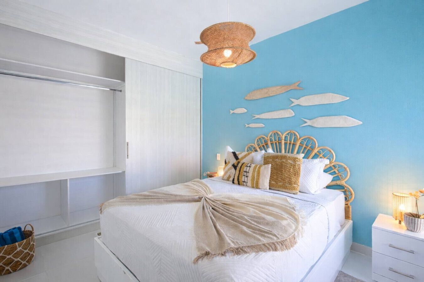 Une chambre à coucher avec un lit, une tête de lit, un luminaire suspendu, un mur décoré de motifs de poissons et une fenêtre.