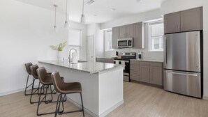 A modern kitchen with a central island, bar stools, stainless steel appliances, and a large refrigerator.