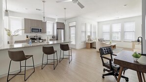Een moderne keuken met een centraal eiland, barkrukken, een eettafel met stoelen en een plafondventilator.