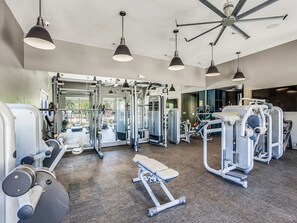 Ein Fitnessraum mit verschiedenen Trainingsgeräten, einer Bank und Pendelleuchten.