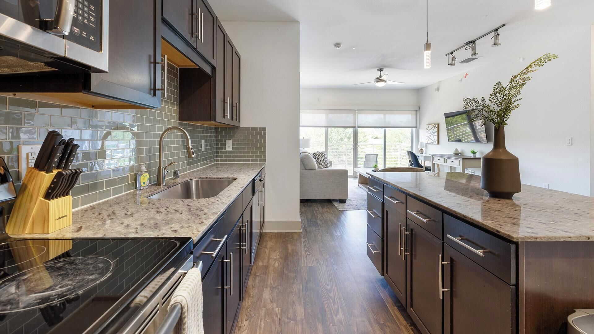 A modern kitchen with dark cabinetry, a stainless steel sink, and a marble countertop.