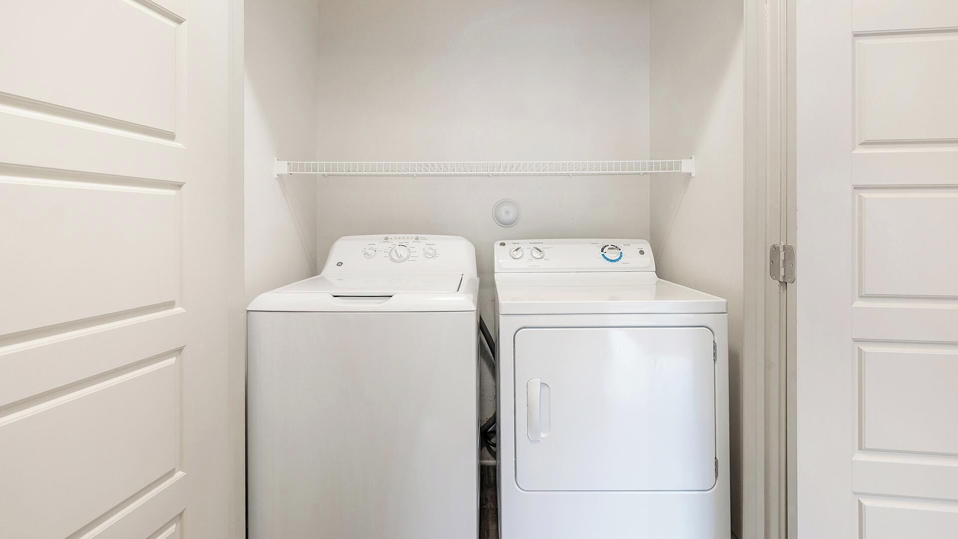 Une buanderie avec deux machines à laver blanches et un sèche-linge, une porte blanche et un mur blanc.
