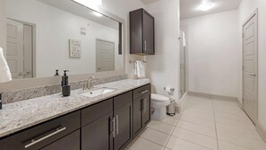 Une salle de bain moderne avec un comptoir en marbre, des meubles sombres, un grand miroir et un espace douche.
