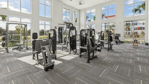 Ett rymligt gym med olika träningsmaskiner, stora fönster och en takfläkt.