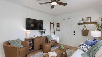 Un salon avec un canapé marron, une table basse en bois, un divan blanc, un ventilateur de plafond et un téléviseur fixé au mur.