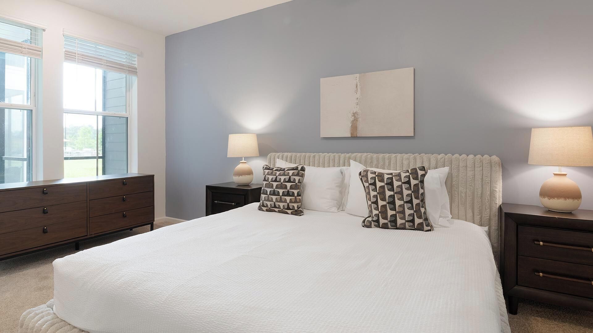 A bedroom with a large bed, two bedside tables, a dresser, and a window.