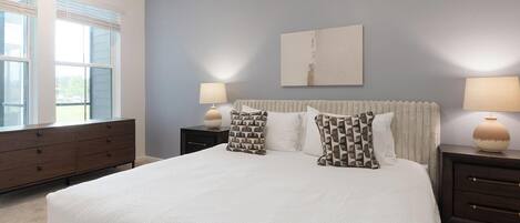 A bedroom with a large bed, two bedside tables, a dresser, and a window.