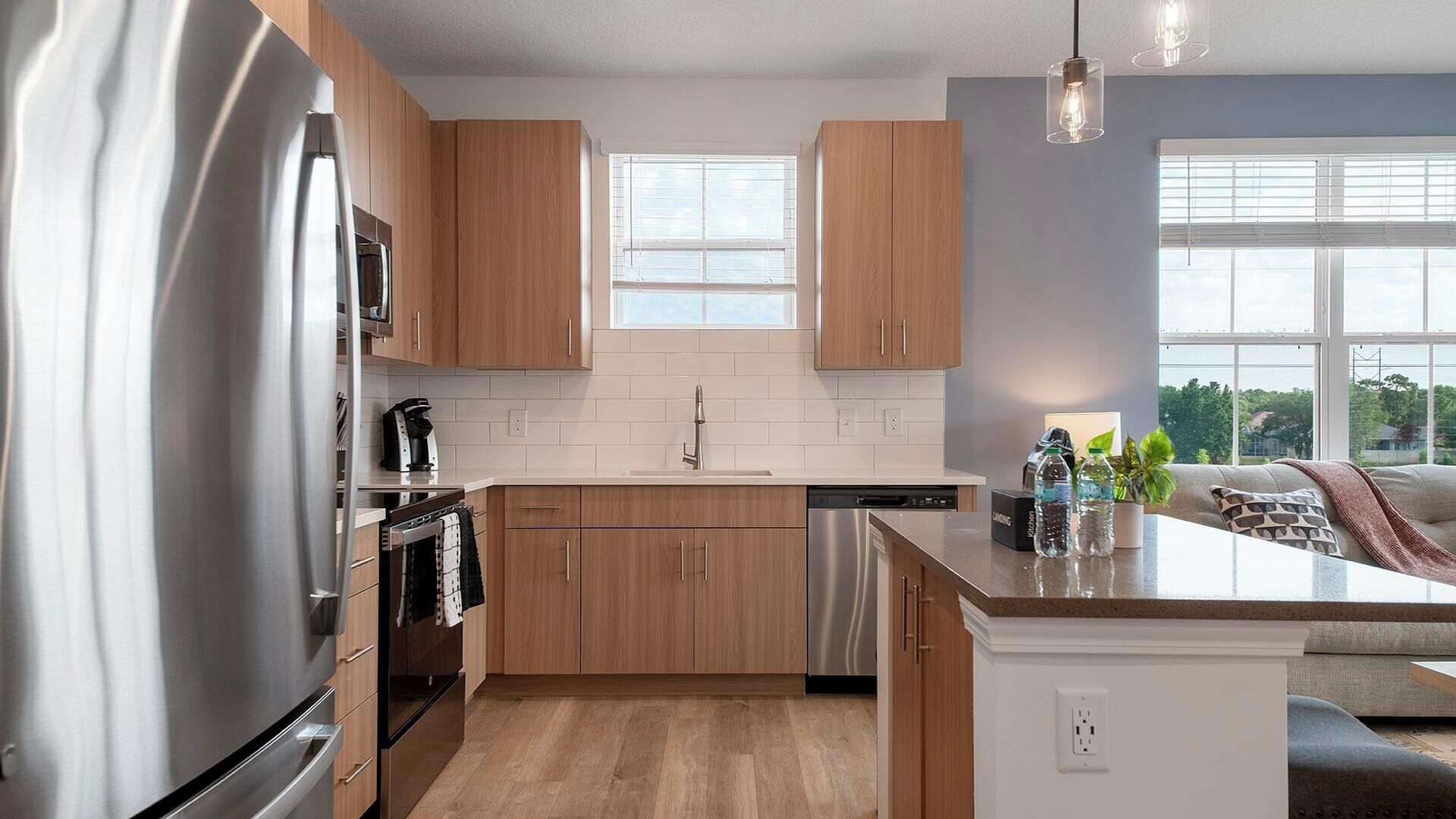 A modern kitchen with wooden cabinets, stainless steel appliances, a central island, and a view of the outdoors.
