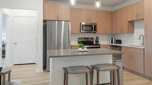 Eine moderne Küche mit Holzausstattung, Edelstahlgeräten und einer zentralen Kochinsel mit Barhocker.