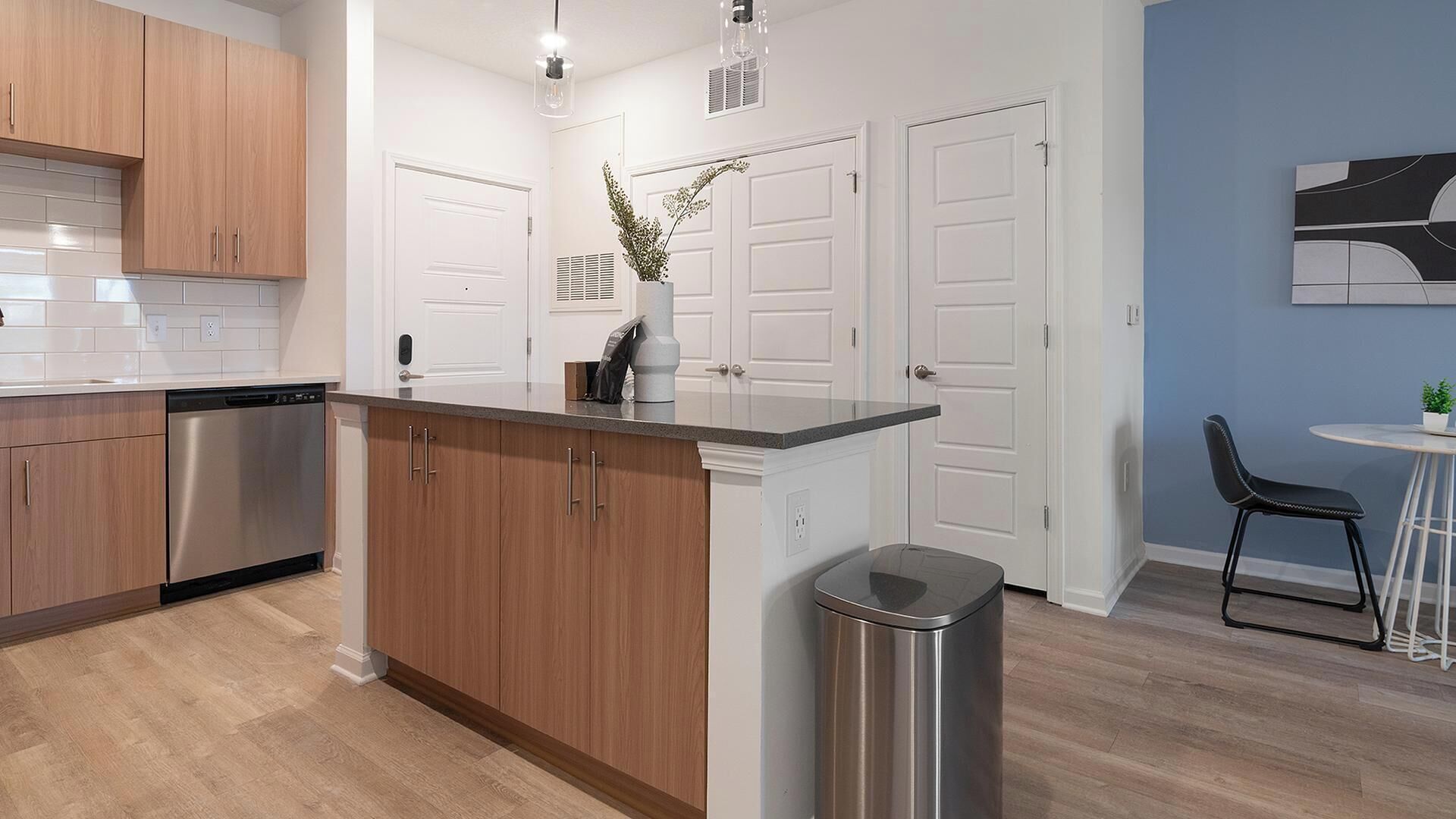 Una cocina moderna con armarios de madera, un lavavajillas de acero inoxidable y un cubo de basura.