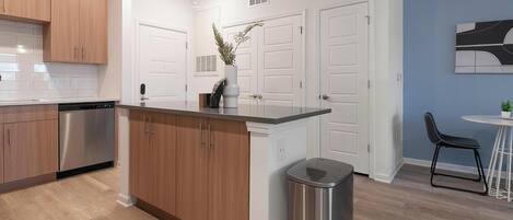 Una cocina moderna con armarios de madera, un lavavajillas de acero inoxidable y un cubo de basura.