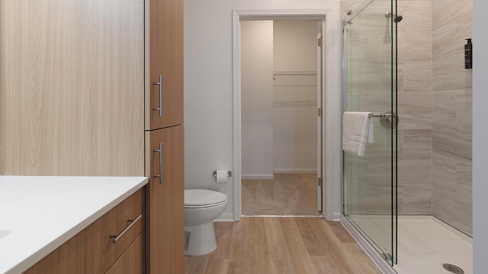 A modern bathroom with a toilet, shower, and wooden cabinets.