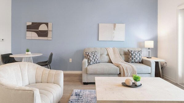 A living room with a sofa, armchair, coffee table, and a small table with a lamp. - Landing | Incredible 1BD, Gym, Clubhouse (Kissimmee)