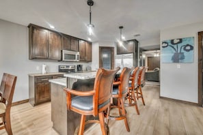 A modern kitchen with wooden cabinets, a central island with bar stools, stainless steel appliances, and a ceiling light fixture.